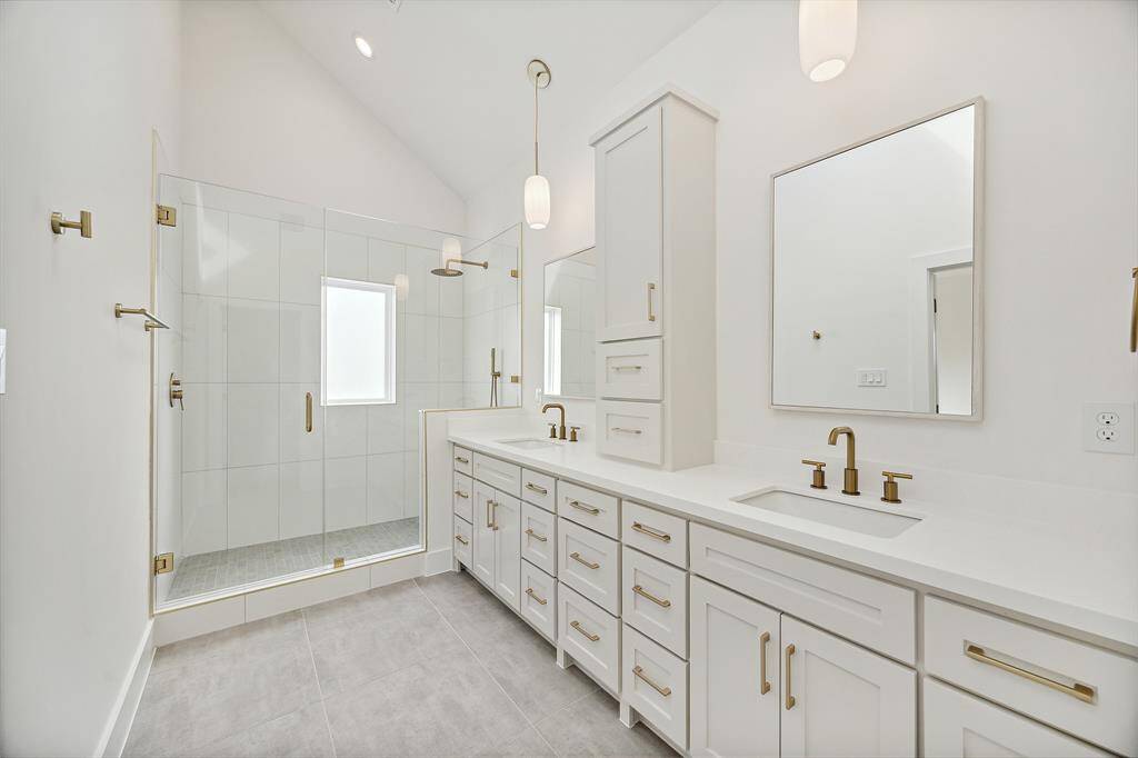 Luxurious primary bath features a vaulted ceiling, sky light, frameless glass walk in shower, dual vanities with coordinating hardware, designer faucets, plumbing accessories, modern light fixtures and separate toilet room