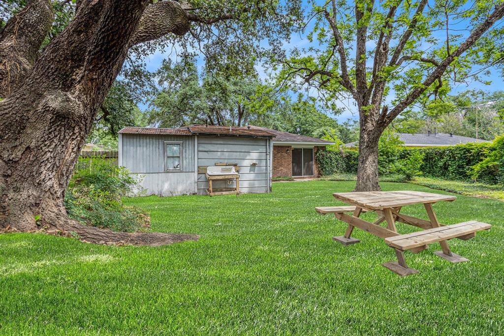 Large back yard with numerous mature shade trees and picnic bench