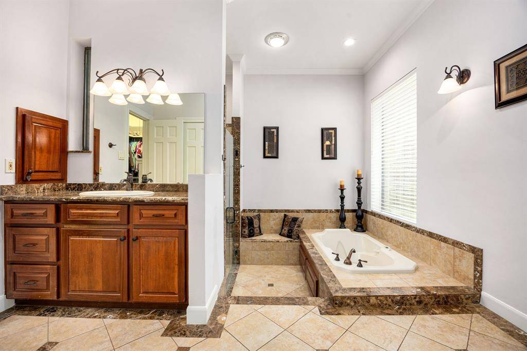 This primary bathroom is definitely move-in ready! Featuring a dark framed walk-in shower with tile surround, separate garden tub for soaking after a long day with custom tile detailing, dark stained cabinets with light countertops, spacious walk-in closet with shelving, high ceilings, custom paint, sleek and dark modern finishes.
