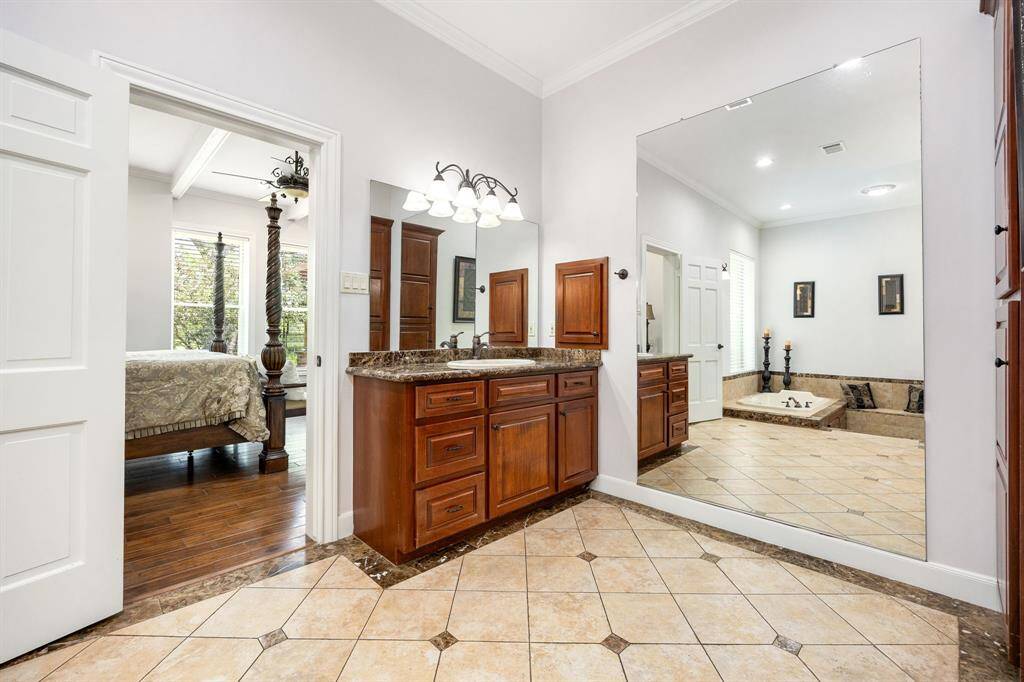 The expansive primary bathroom offers dual vanities with rich wood cabinetry, sleek granite countertops, and a wall-to-wall mirror that enhances the room’s brightness and sense of space, perfect for a luxurious daily retreat.