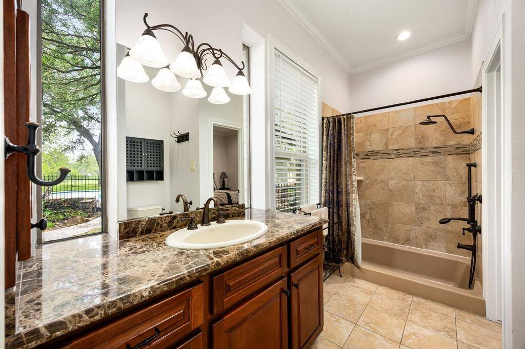 Secondary bath features tile flooring, bath/shower combo with tile surround, dark wood cabinets, beautiful light countertops, mirror, dark, sleek fixtures and modern finishes.