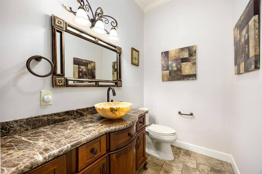 This elegant half bath features a rich granite countertop, a striking vessel sink, ornate fixtures, and stylish decor offering guests a luxurious and welcoming space.