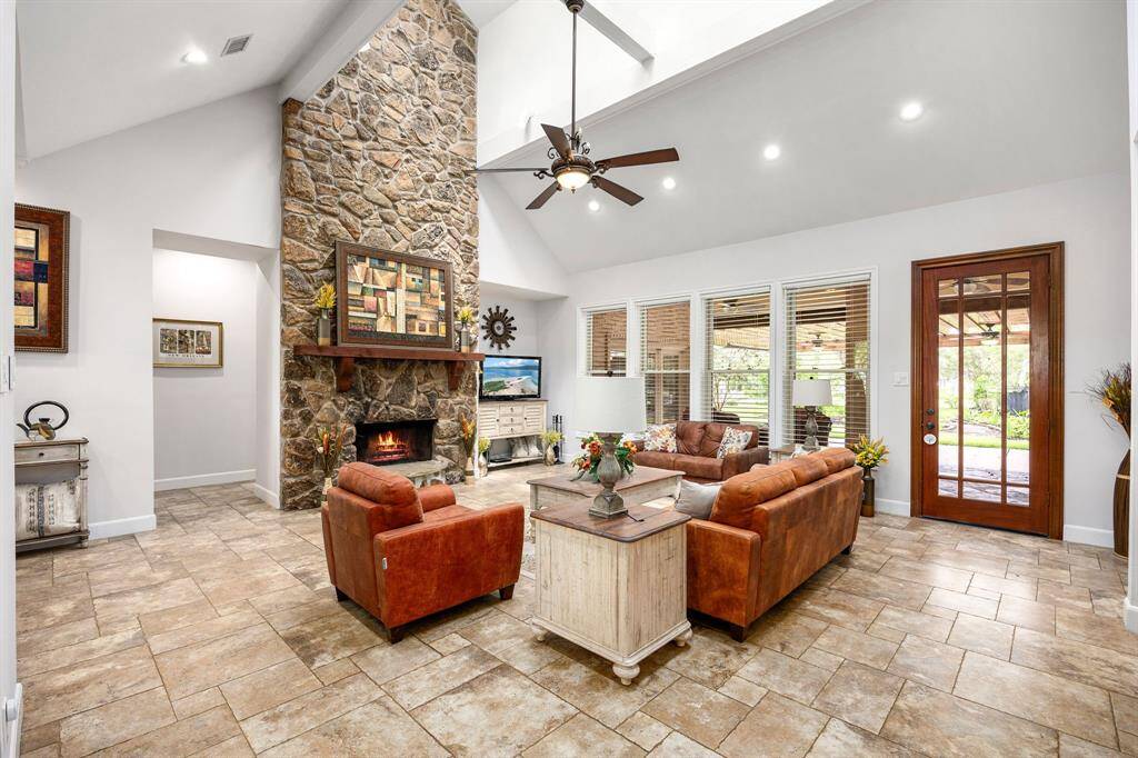 This living room is more like a GREAT room featuring a stunning fireplace with mantel detailing, custom paint, soaring high ceiling, recessed lighting, dark stained ceiling fan, and an amazing wall of windows providing a lovely view of your backyard to keep an eye out on the kids or pets playing.