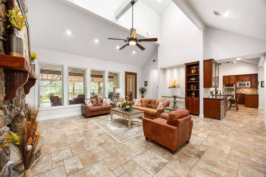 Welcome to your new favorite hang out spot! This stunning living room boasts soaring ceilings, elegant recessed lighting, a rich dark-stained ceiling fan, beautiful tile flooring, custom paint, and expansive windows that flood the space with natural light all day long.
