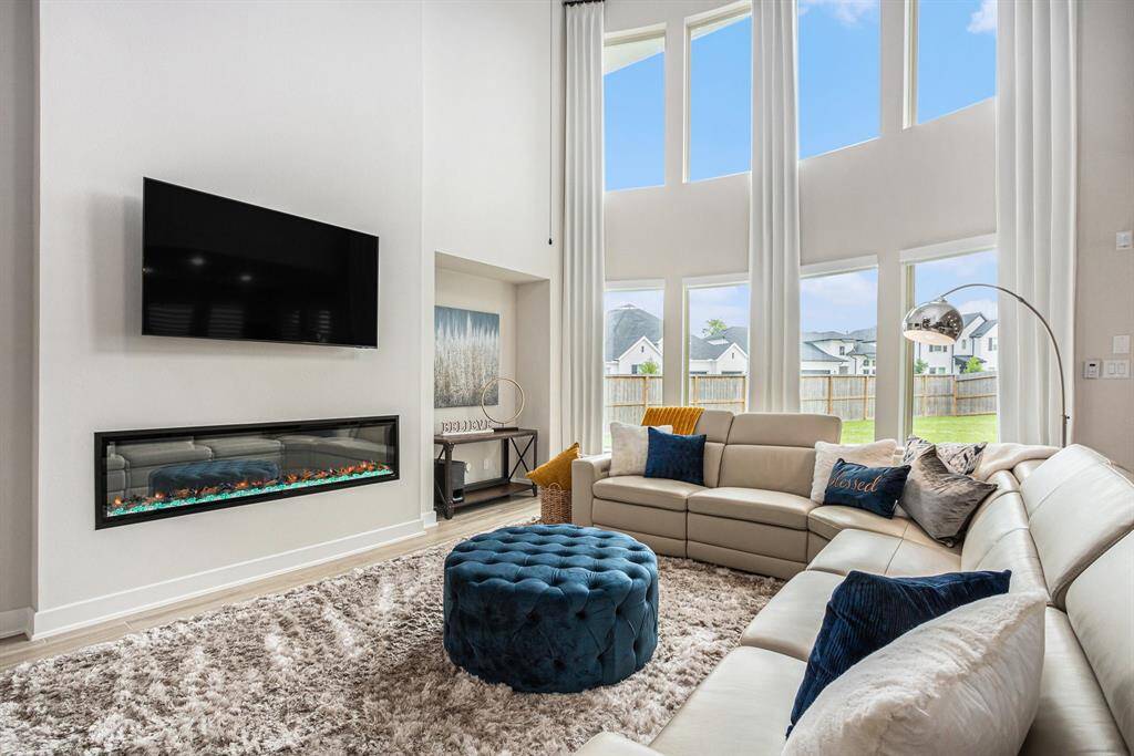 Living room with plenty of natural light, an electric fireplace and high ceilings.
