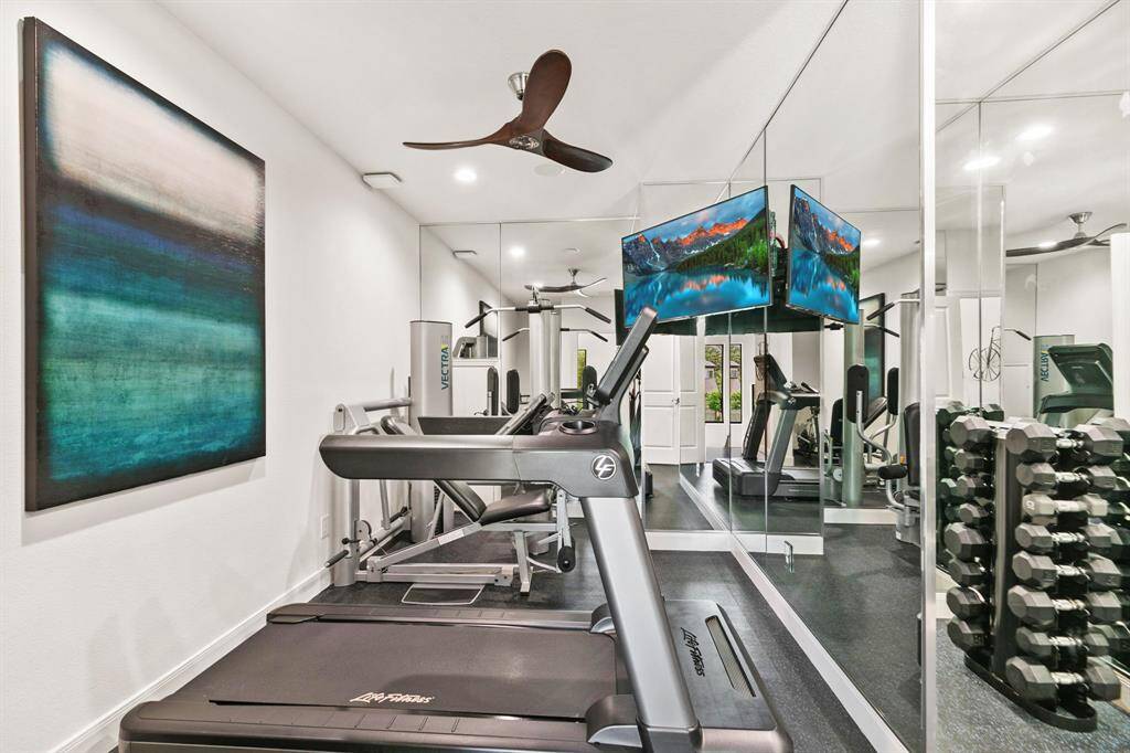 The home gym is surrounded by mirrors and features a ceiling fan and TV.