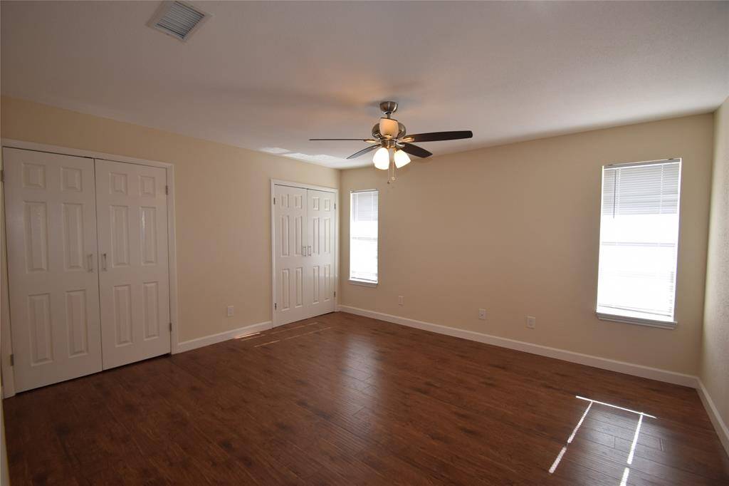 Master bedroom upstairs offering hardwood laminate floors, two closets, ceiling fan with light fixture and window blinds.