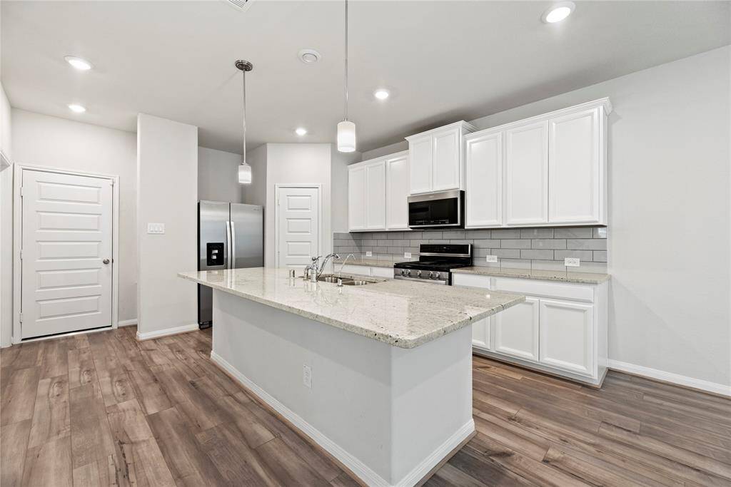 The modern kitchen features white cabinets, an oversized island, stainless steel appliances, and lots of lighting.