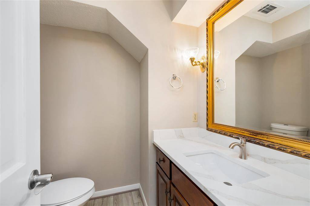 This secondary half bath features thoughtful updates, including sleek upgraded countertops, an expansive framed mirror that enhances the space, and elegant light fixtures that add a touch of sophistication. It’s a beautifully designed space that combines style with function, making it perfect for guests.