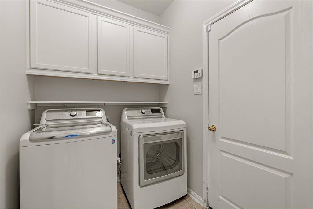 The spacious laundry room is complete with painted white cabints, additional shelving, and a washer and dryer.
