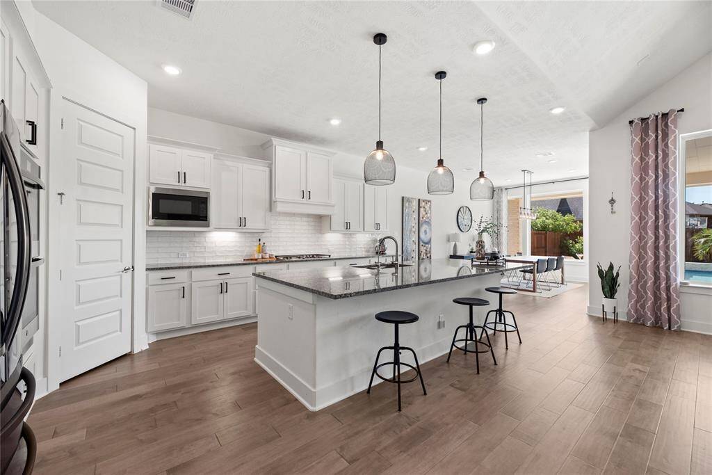 The chef’s kitchen is equipped with ample counter space, luxurious granite countertops, subway tile backsplash, and top-of-the-line stainless steel appliances, including double ovens.