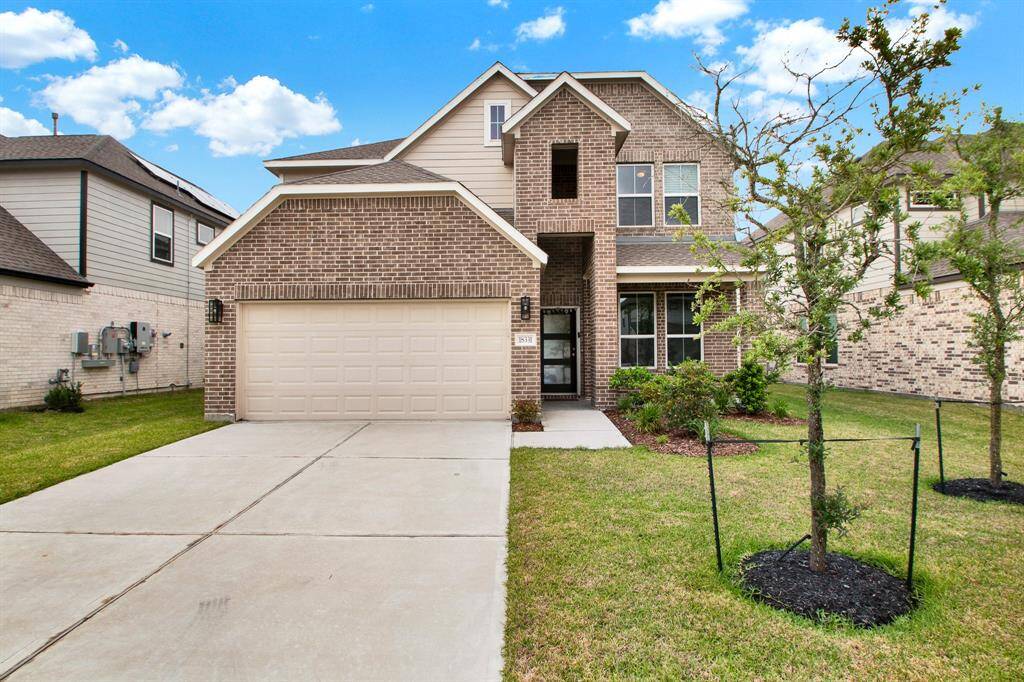 This two-story brick home has a spacious driveway leading to a two-car garage. The front yard is neatly landscaped with trees and shrubs. The house has a clean, contemporary design with large windows and a welcoming entrance.