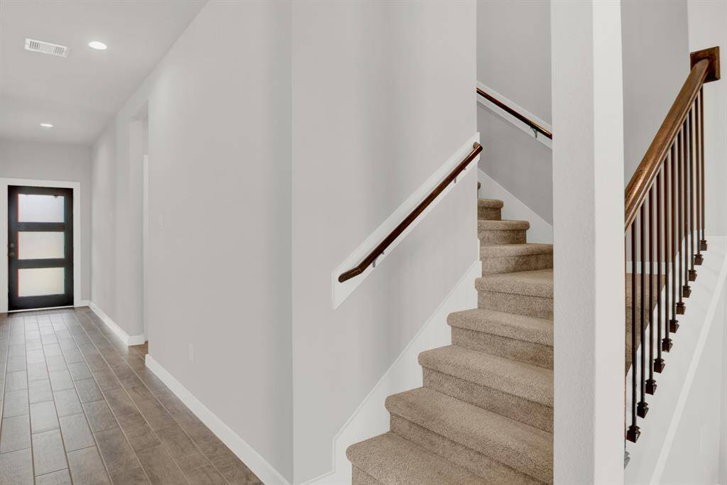 Modern entryway with recessed lighting leading to a carpeted staircase with wooden handrails.