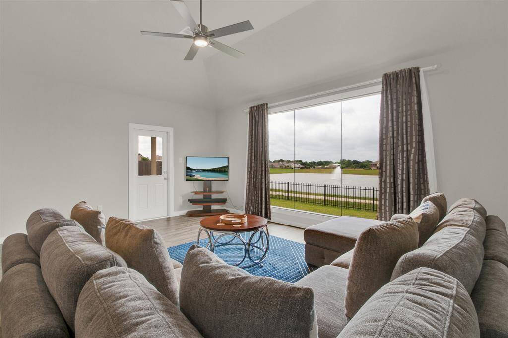 Bright living room with large windows offering a scenic view of a pond and fountain. Ideal for relaxation and enjoying the outdoors from inside.