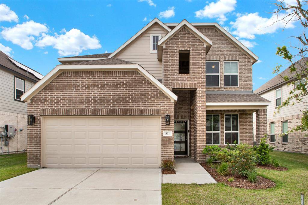 This two-story brick home has a spacious driveway leading to a two-car garage. The front yard is neatly landscaped with trees and shrubs. The house has a clean, contemporary design with large windows and a welcoming entrance.