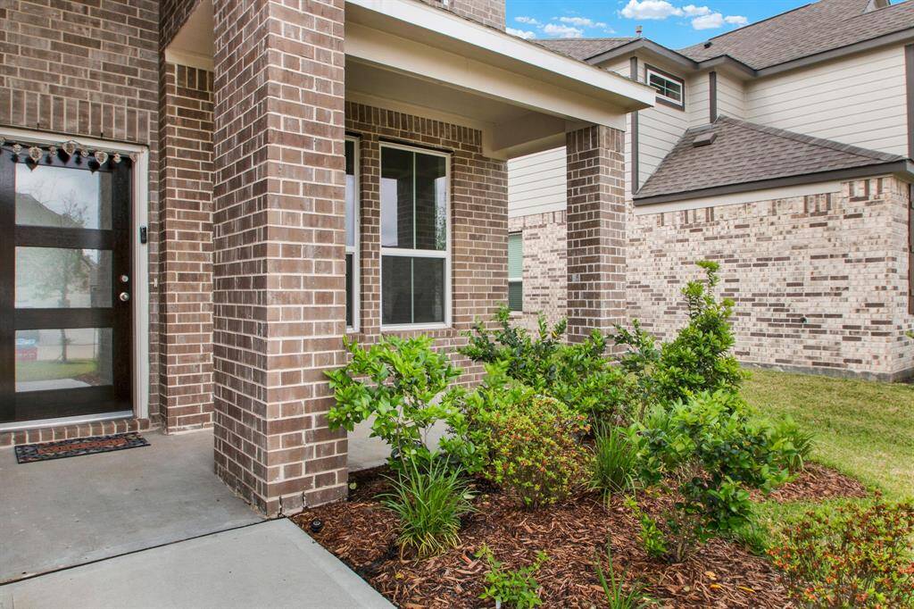 The home's entrance features a covered porch and the front door features glass panels, and there's a well-maintained garden with shrubs.