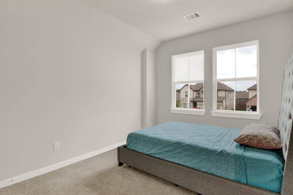 This bedroom features neutral-toned walls and carpet, and a large windows providing natural light. It's a cozy space with a view of the neighborhood.