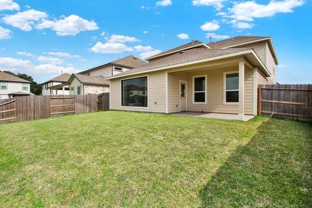 Spacious backyard with a well-maintained lawn, a wooden fence for privacy, and a covered patio attached to a modern two-story house. Perfect for outdoor activities and relaxation.