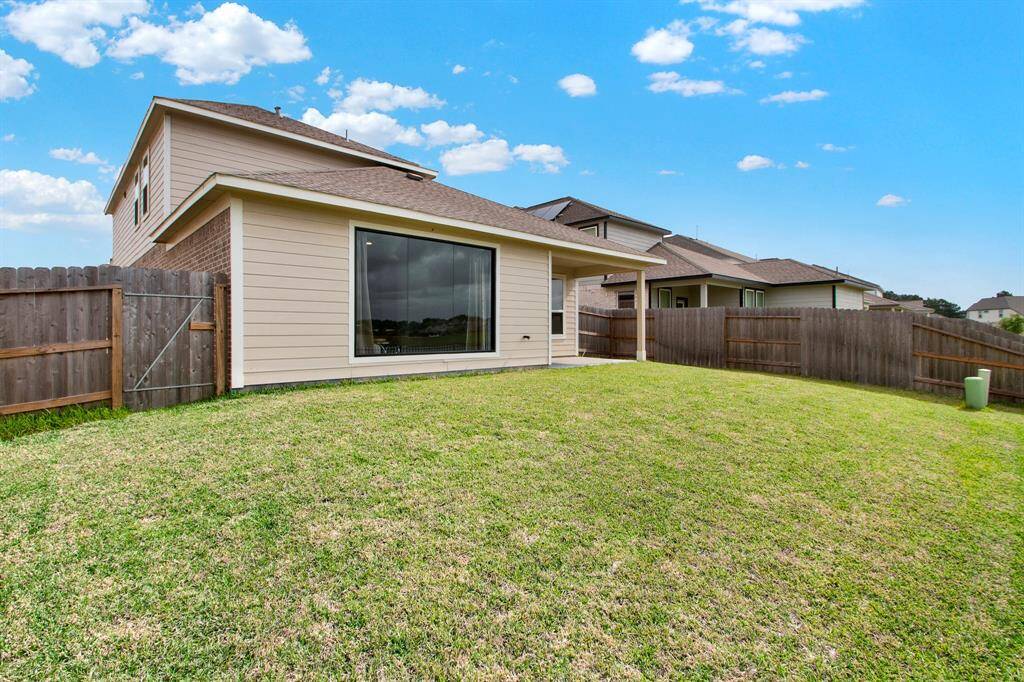 Spacious backyard with a well-maintained lawn, a wooden fence for privacy, and a covered patio attached to a modern two-story house. Perfect for outdoor activities and relaxation.
