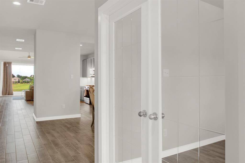 Modern, open-concept interior with wood-style flooring and lots of natural light. It features a view of the living room, a kitchen area, and glass double doors leading to another room.