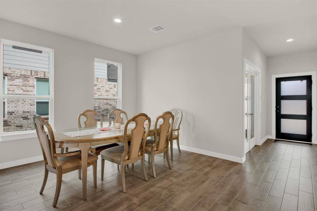Bright, open dining area complemented by large windows that allow natural light to fill the space. The room has a modern design with light walls and a stylish entry door, perfect for family gatherings.