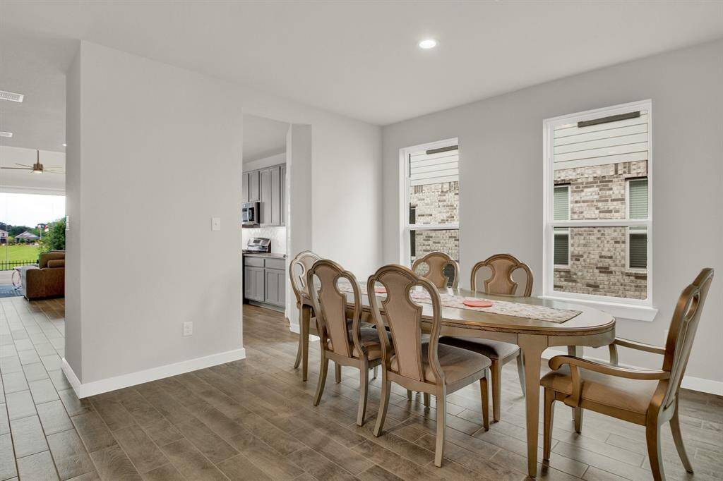 Bright dining area featuring large windows that bring in natural light. The space connects to the kitchen with gray cabinets and an open living area, creating a seamless flow ideal for entertaining.