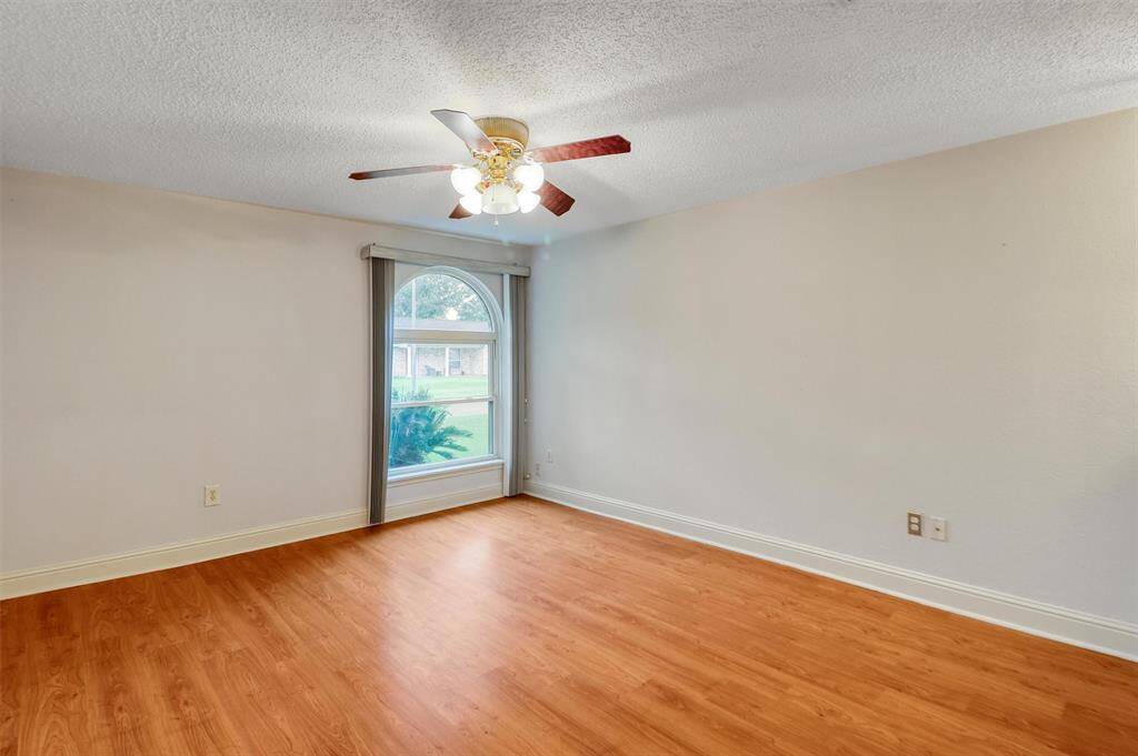 This primary bedroom features a bright, open space with laminate wood flooring and a large window for natural light. The ceiling fan adds comfort, making it an inviting area for relaxation.