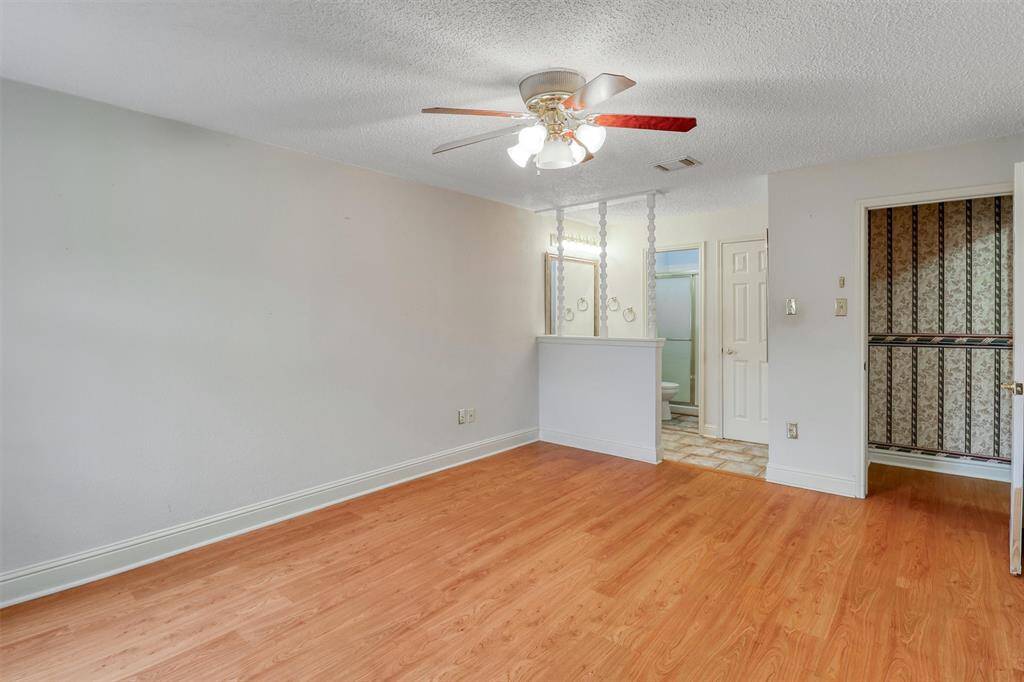 This primary bedroom features laminate wood flooring and a ceiling fan, with an open view into an ensuite bathroom area. It has neutral walls and a decorative partition, creating a cozy, inviting space.
