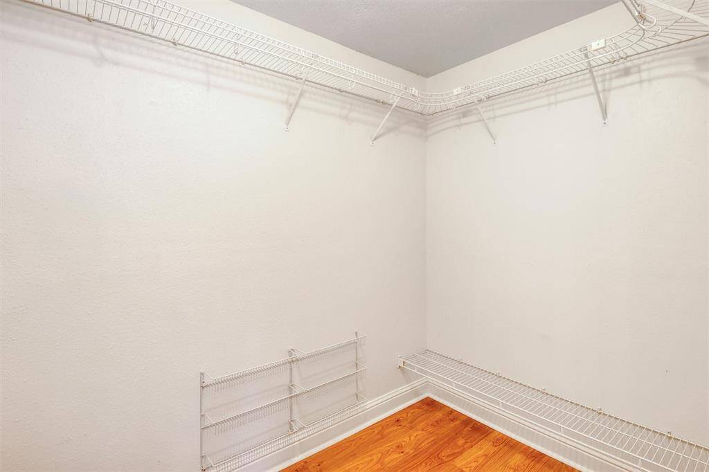 This photo shows a spacious walk-in closet in the primary bedroom with white wire shelving, offering ample storage space. The closet has a light, neutral color scheme and a laminate wood floor.