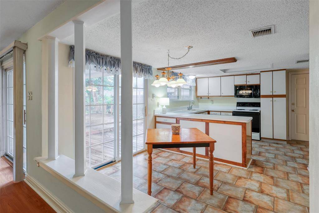 This photo shows a bright kitchen with white cabinetry and vinyl flooring. It features a breakfast area and large sliding glass doors that open to a deck, providing plenty of natural light.