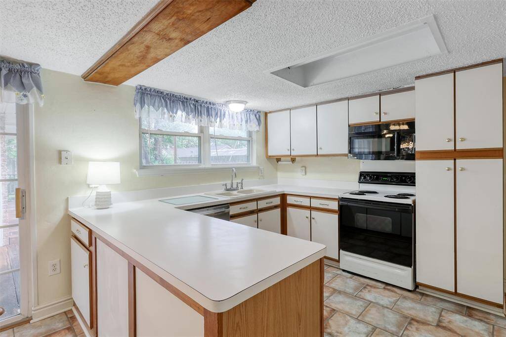 Bright kitchen with natural light, featuring white cabinetry and countertops, a black stove and microwave, and patterned vinyl tile flooring. The space includes a cozy breakfast area and ample storage.
