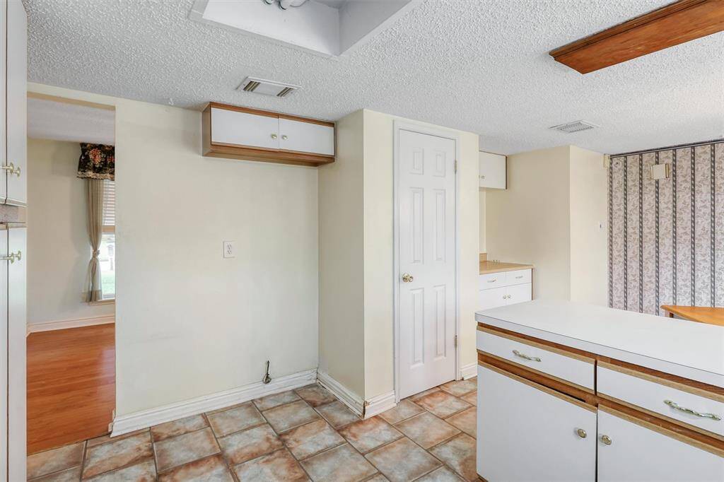 This kitchen features a cozy layout with vinyl tile flooring, ample storage, light cream walls, and wooden accents. It includes a small pantry, built-in cabinets, and leads to a family room with laminate wood floors and natural light.