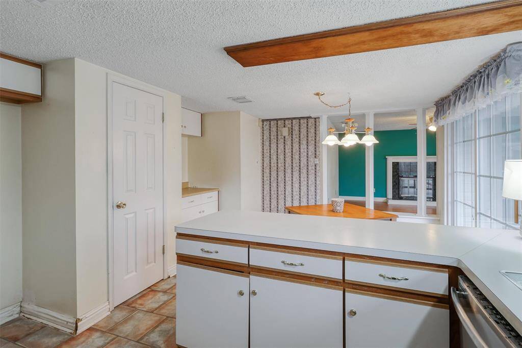 Bright kitchen with a cozy breakfast area, featuring a formica countertop and ample cabinetry. The space is accented by a hanging light fixture and large windows, offering plenty of natural light.