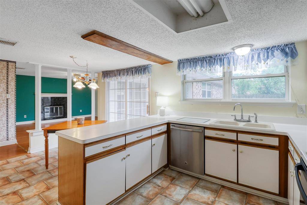Bright kitchen with ample counter space and a cozy breadfast area. Large windows provide natural light, and there's a view into the living room with a wood burning fireplace.