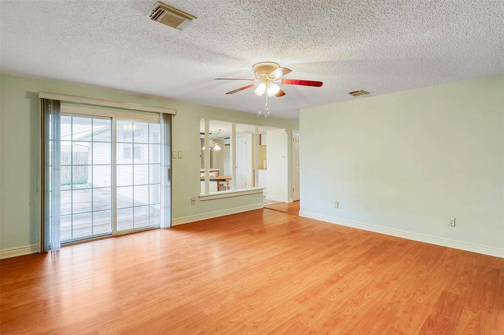 This spacious family living room features laminate wood flooring, a ceiling fan with lights, and a large sliding glass door leading to a deck, bringing in abundant natural light. The open layout includes a view into the adjoining kitchen and dining area.