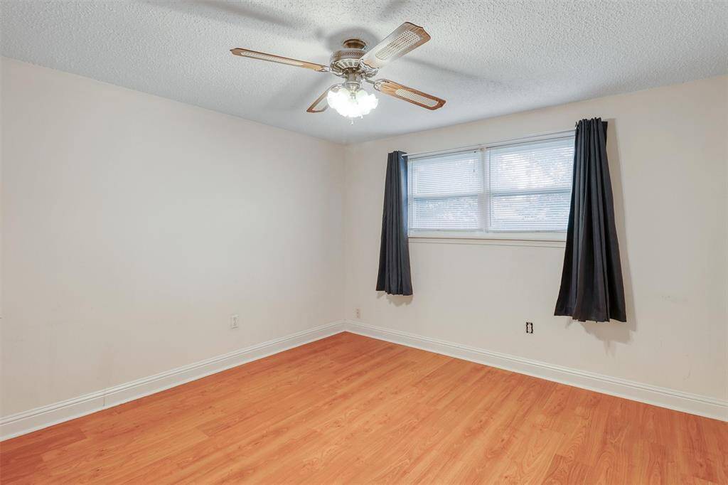 This room features laminate wood flooring, a ceiling fan with lights, and a window with dark curtains, offering a cozy and bright space.