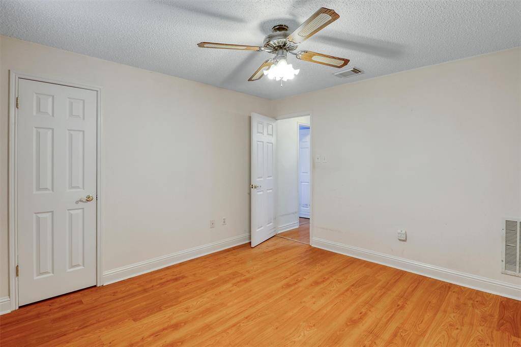 This room features laminate wood flooring, a ceiling fan with lights, and neutral walls. It includes two doors: one for a walk in closet and one leading to a hallway. Ideal for a bedroom or office space.