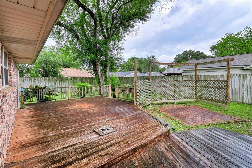 Spacious backyard deck with a wooden fence, surrounded by greenery and shade from mature trees, offering a great area for outdoor entertaining.