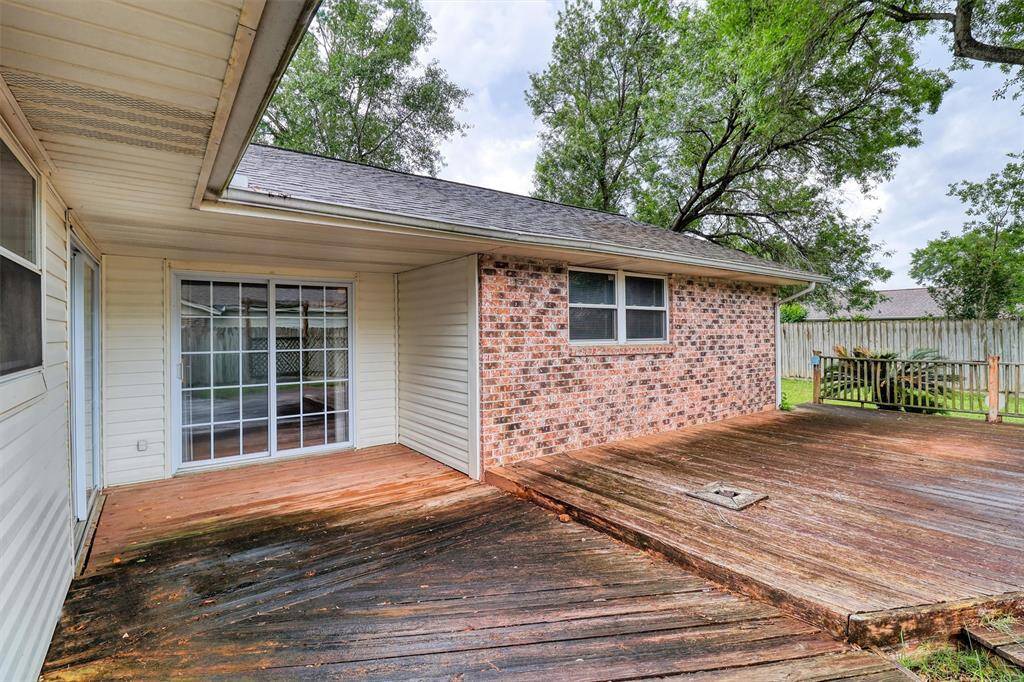 This photo showcases a backyard with a spacious wooden deck, ideal for outdoor gatherings and is enclosed by a wooden fence, providing privacy. Lush greenery and mature trees offer a serene ambiance.