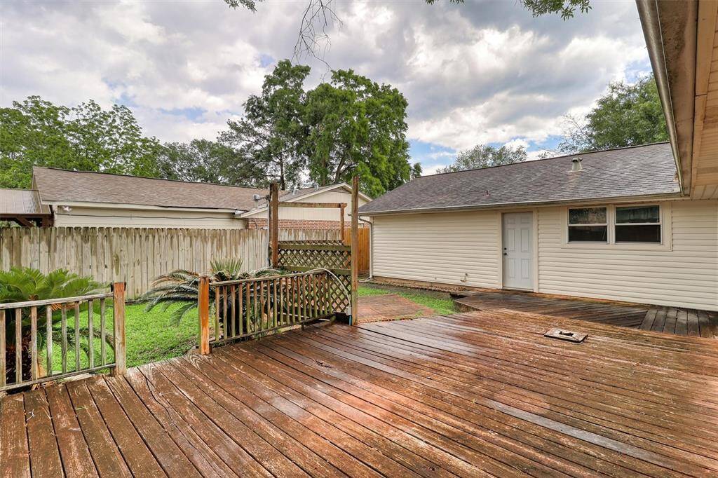 Charming backyard featuring a spacious lawn, mature trees for shade, and a privacy fence. The side of the brick house is visible, offering potential for landscaping and outdoor activities.