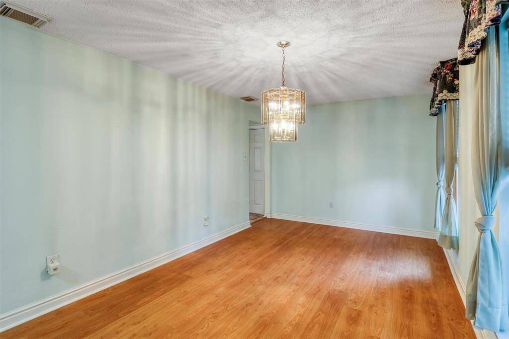 Bright dining or optional flex area with laminate wood flooring, light walls, and an elegant chandelier. Large windows with decorative curtains allow natural light to fill the space.