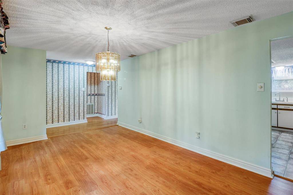 This is a cozy dining or optional flex area featuring laminate wood flooring and a stylish light fixture. It opens to a kitchen with a view of the sink and cabinets, and there's a decorative wall and trim detailing on one side.