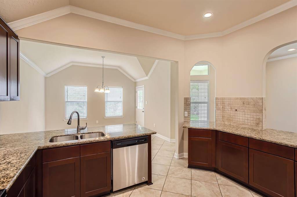 This kitchen features granite countertops, dark wood cabinetry, and stainless steel appliances. The open design flows into a bright dining area with large windows, vaulted ceilings, and elegant tile flooring.