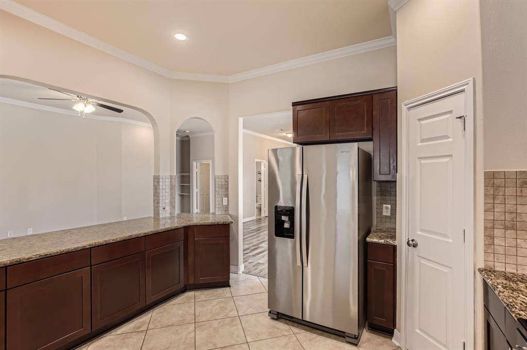 This kitchen features stainless steel appliances, granite countertops, and dark wood cabinetry. It opens into a spacious living area with an arched entryway and ceiling fan, creating a warm and inviting space.