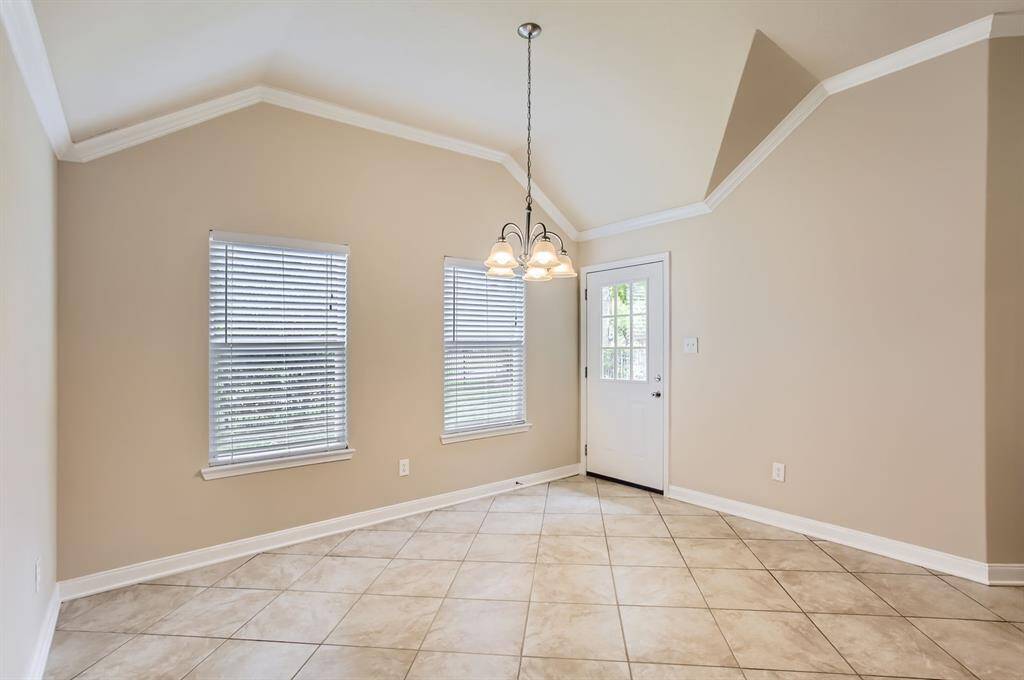 Bright living area with high ceilings, neutral walls, and tiled floors. Features large windows with blinds, a stylish light fixture, and a door leading outside.