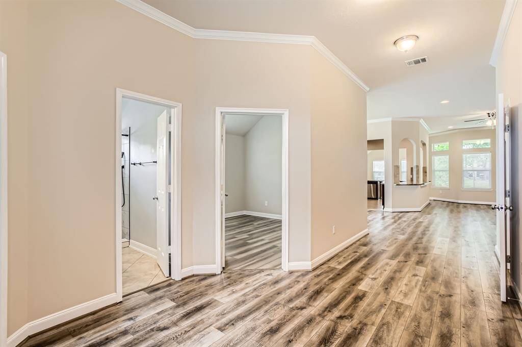 Spacious and bright hallway with wood flooring and neutral walls, leading to multiple rooms. An open layout connects to a kitchen area with large windows providing ample natural light.