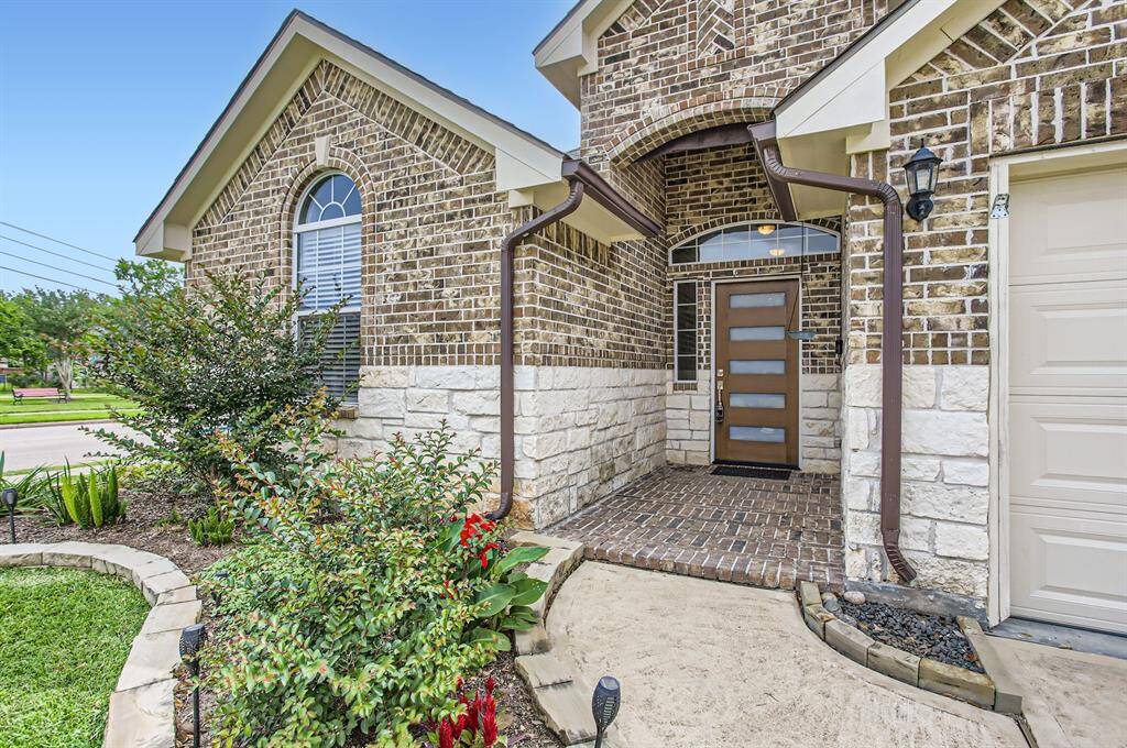 This photo showcases the front entrance of this charming brick home. It features a modern door, a well-maintained walkway, and attractive landscaping with lush greenery and vibrant flowers. The exterior blends brick and stone for a classic yet contemporary look.