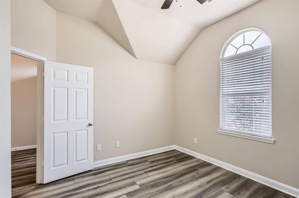 This bedroom features high ceilings and a large arched window with blinds, offering natural light. It has neutral-toned walls, wood-like flooring, and a white door, creating a bright and airy space.
