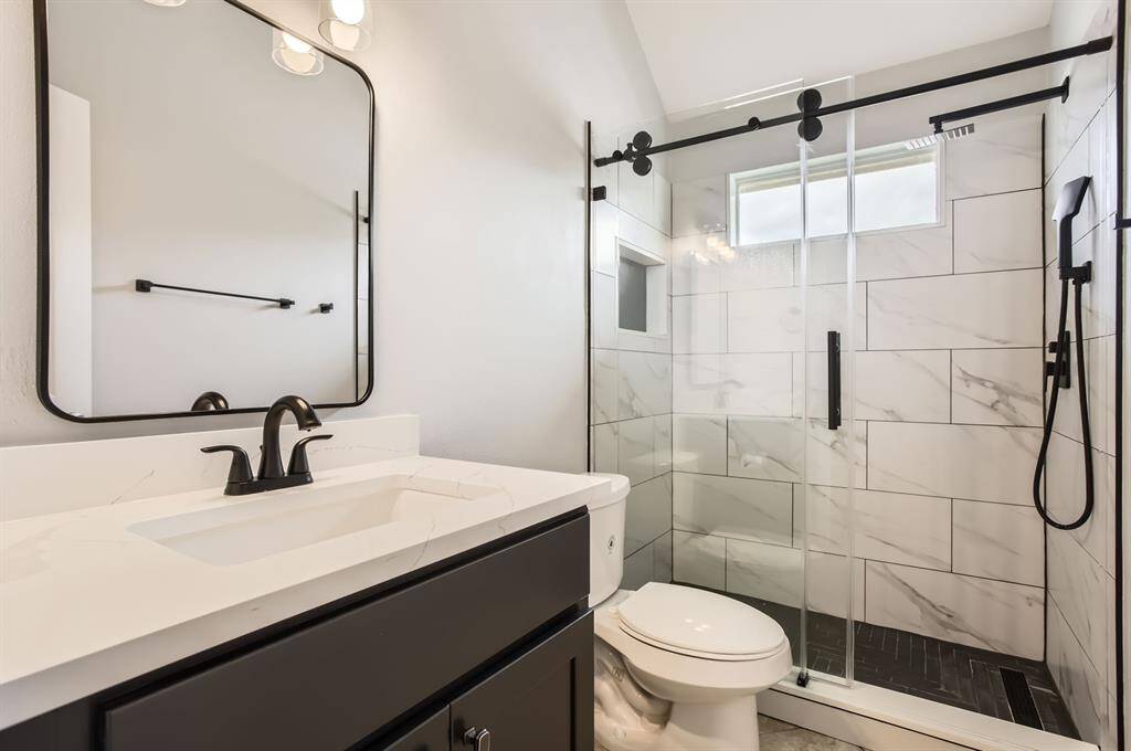 Modern second bathroom with a sleek design featuring a large mirror, black fixtures, and a spacious glass-enclosed shower with white marble tiles.