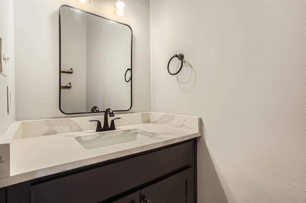 This half bathroom features a modern vanity with a white countertop, a sleek black faucet, and a large, stylish mirror. The neutral tones and simple design create a clean, contemporary look.